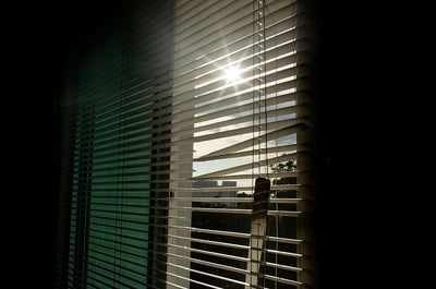 broken blinds in dark room with sun shining in